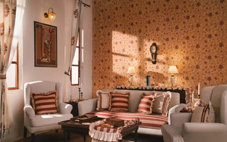 A drawing room composed for English high tea decor, with small-floral wallpaper, a striped sofa and ruffled cushions under lamplight