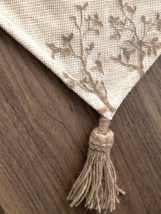 A macro shot highlighting the thick, hand-knotted rustic jute tassel and braided edge piping of the Rooted Grace table runner.