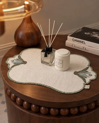 A Barg placemat in Moss & Teal on a side table beneath a diffuser, candle and stacked books.