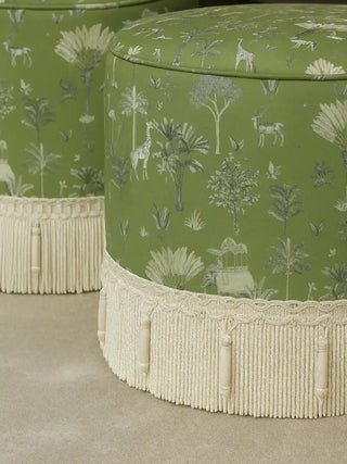 Luxury round ottomans upholstered in Itihaas design sage green velvet featuring a fringed base and royal safari motifs.