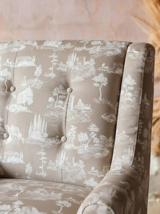 A close-up of Chic Toile light brown velvet fabric used on a button-tufted armchair featuring white neoclassical landscape motifs.