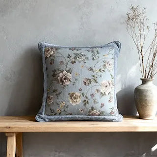 Blue floral cushion with ornate trim on a wooden bench.