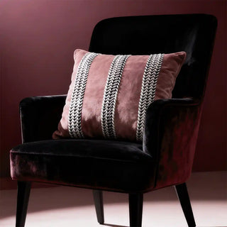 Blush Braid Cushion Cover: A plush pink velvet cushion adorned with bold black and white braided stripes, exuding moody sophistication. Styled on an armchair.