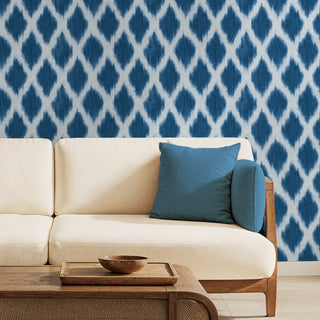 A blue ikat wallpaper with a diamond pattern on a wall behind a beige sofa and wooden coffee table, perfect for a modern living room wallpaper.