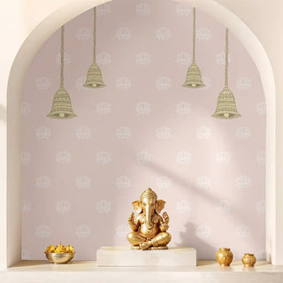 Gold Ganesh statue on a white pedestal with hanging decorative bells against a patterned wallpaper