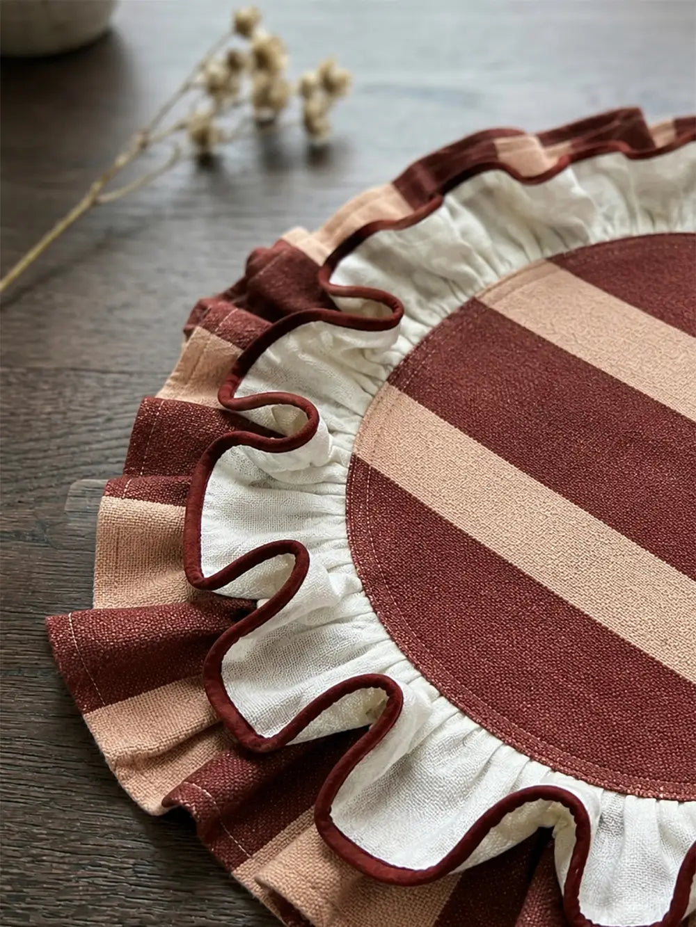 Close detail of a cream linen placemat with hand-finished ruffle border and a striped band