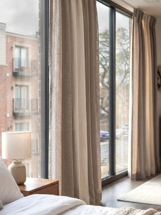 he Kanan curtains elegantly framing a large bedroom window. It highlights the beautiful full-length drape, clearly displaying the striking design: a solid off-white ivory linen center framed by sophisticated, textured mesh borders that softly filter the natural light.
