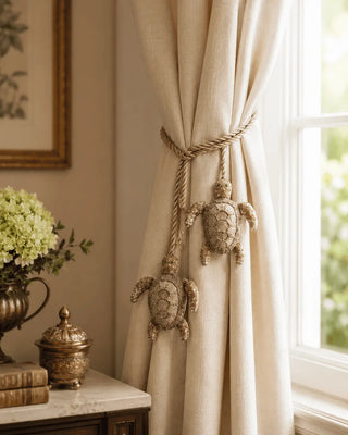 Hand-beaded Kurma turtle charm holding back a cream linen curtain beside a sunlit window