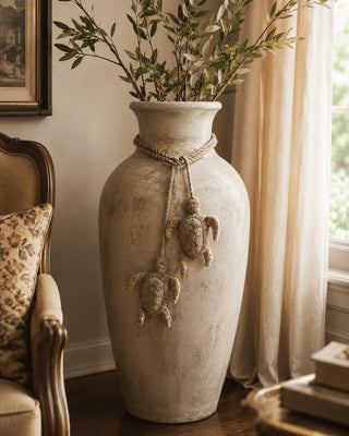 Beaded Kurma turtle charm tied around the neck of a tall stone floor vase