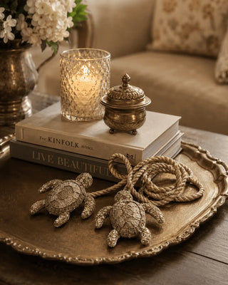 Two hand-beaded Kurma turtle charms with rope cord styled on a gold tray with books