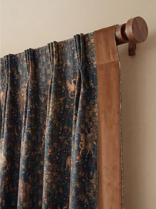 focused close-up of the top header of a Majestica curtain. This perspective clearly shows the tailored pinch pleats and the dark turned wood rod. The seam where the deep blue fantasy print center meets the rich brown...