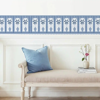 Beige sofa with a blue pillow and a vase with flowers against a white wall with decorative blue border wallpaper