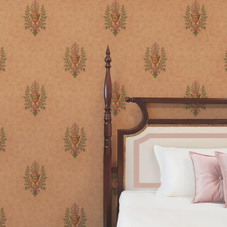 A bedroom wall featuring a traditional Indian-style wallpaper with a repeating pattern of floral motifs in urns on a tan background.