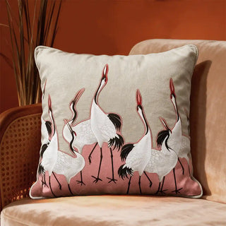 Sedge Pink Cushion Cover: Featuring embroidered cranes set against a soft pink fabric patch, it pairs beautifully with a warm beige base for a refined, modern contrast. Styled on a sofa in moody environmemt.
