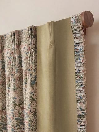 A focused view of the curtain's top edge, illustrating the professional pinch-pleat tailoring on the floral center. The header hangs smoothly from a dark, turned wood rod, displaying the seamless architectural transition from the pleated floral fabric to the smooth solid side panel and the decorative floral ruffle on the outer edge.