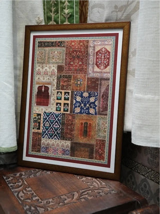 Aalishan Mughal carpet patchwork wall art in a dark wood frame, leaning on a carved wooden floor beside a white linen curtain.