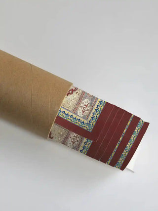 Aalishan wall art partially unrolled from its kraft paper shipping tube, revealing the crimson border, teal floral vine frame, and antique carpet patchwork detail