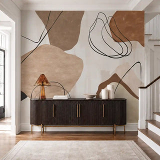 The Abstract Ochre wallpaper mural installed behind a dark wood ribbed console with a staircase and amber table lamp view-foyer