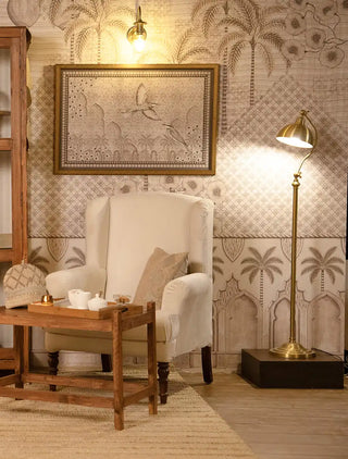 The Alhambra's Whisper wallpaper mural with palm trees, pointed arches and lattice, behind a cream wingback chair, wooden tea table and brass floor lamp.