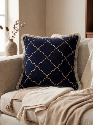 A lifestyle view of the Amer Lattice navy blue cushion styled on a beige sofa next to a linen throw.
