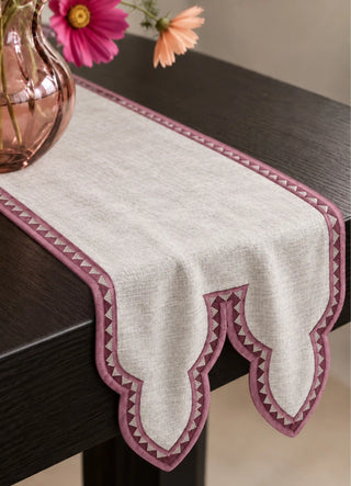 The Amrah Runner in Natural & Mauve drapes over a dark wood console, styled with a pink glass vase of cosmos flowers, showing the cusped double-point tail end.