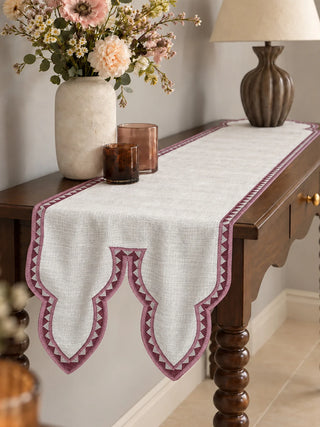 The Amrah Table Runner in Natural & Mauve runs along a dark wood console styled with a stone vase, amber glass candles and a carved lamp base.