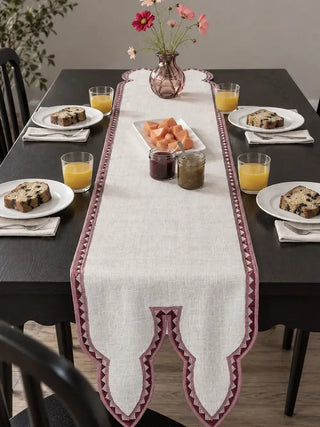 The Amrah Table Runner in Natural & Mauve centres a dark wood dining table set for breakfast with loaf cake, orange juice and fruit preserves.