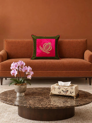 The Anarkali cushion cover on a rust velvet sofa against a terracotta wall, a gold pomegranate on fuchsia velvet inside an olive green border.
