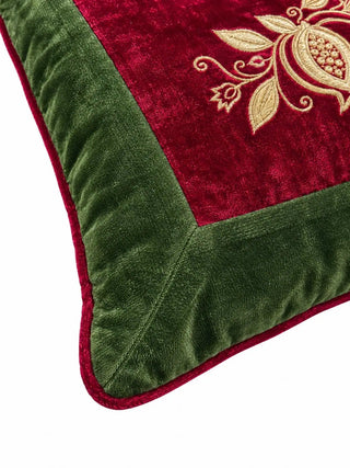 Close-up of the Annar Bagh cushion corner: a gold-embroidered pomegranate on red velvet, a mitred olive green velvet border and red piping.