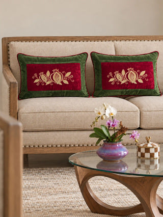 Two Annar Bagh lumbar cushion covers on a cream sofa with a wooden frame, red velvet panels with gold pomegranates framed in olive green velvet.