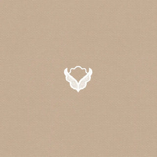 A detailed close-up highlighting the ivory emblem motif and the warm beige linen-texture of the Anuraag wallpaper.