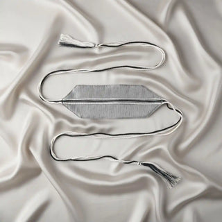 Flat lay of the Ashline Handcrafted Curtain Tieback showing the grey geometric panel and braided tassel cords on a silk background.