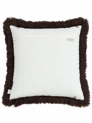 The back of the Aurea cushion cover: a plain ivory panel with an overlap seam, a brand label and a dry clean only care label, ringed by deep brown fringe.
