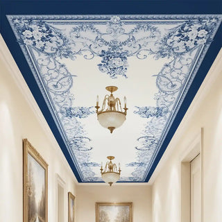 Aurelia Hall Ceiling Wallpaper in a hallway with gold lighting, showing the blue and white neoclassical floral mural.