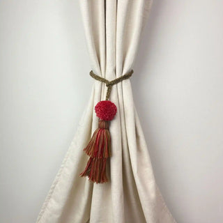 Autumn Flame Handcrafted Curtain Tieback secured around a cream-colored curtain, showing the braided cord and red/gold layered tassel.