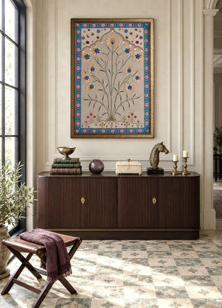 The Bagh-e-Noor embroidered wall art framed above a fluted wood console with brass candlesticks and a sculpted horse head in a sunlit foyer.