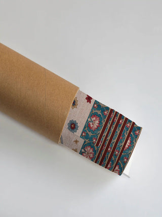 The Bagh-e-Noor wall art print partly unrolled from its shipping tube, showing a floral buti field beside a scrolling floral panel in teal, maroon and cream.