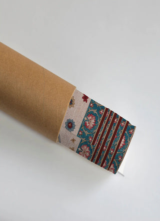 The Bagh-e-Noor wall art print partially unrolled from its kraft paper shipping tube, showing a scattered floral buti field beside a scrolling floral panel in teal, maroon and gold.