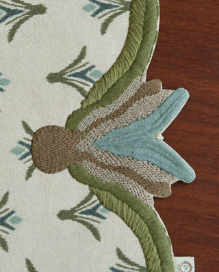 A close-up of the Barg table runner's embroidered leaf finial and beaded tassel in Moss & Teal.