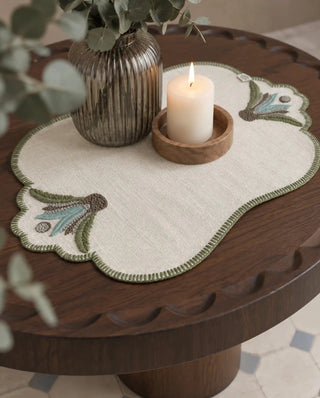 A Barg placemat in Moss & Teal styled with a lit candle and eucalyptus stems on a wooden table.