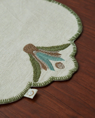 A detailed close-up of the Barg table mat in Sage & Teal highlighting the corner leaf sprig embroidery and hand-stitched edge.