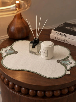 A Barg table mat in Sage & Teal styled on a wooden nightstand with a reed diffuser and stacked books.