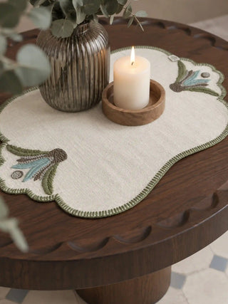 The Barg table mats in Sage & Teal styled on a round side table with a ribbed glass vase and lit candle in a wooden bowl.