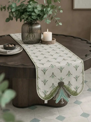 The Barg table runner in Sage & Teal styled on a round coffee table with a ribbed glass vase and lit candle.