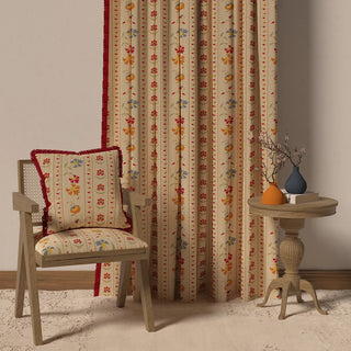 The Bela Fringes curtain displayed in a room setting with a chair and side table, demonstrating its full length and cheerful appearance.