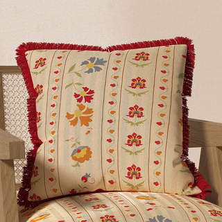 The Bela Fringes cushion cover displayed on a wooden chair, showcasing how its floral pattern and red fringe complement a home decor setting.