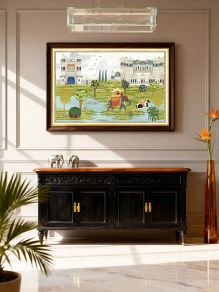 A framed Bharat Rajasthani King mural in a sunlit foyer above a wooden console table with floral vases.