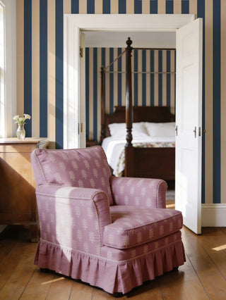 A luxury armchair upholstered in Bloomark lilac fabric with an ivory floral buti pattern, set against navy blue striped wallpaper.