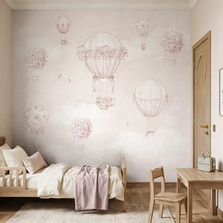 A vintage-inspired floral hot air balloon wall mural in soft pink behind a wooden toddler bed.