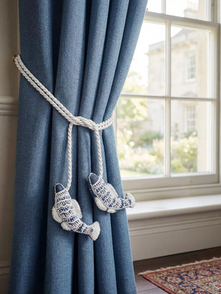 Luxury blue curtains held back by hand-embroidered fish charms on a white braided rope
